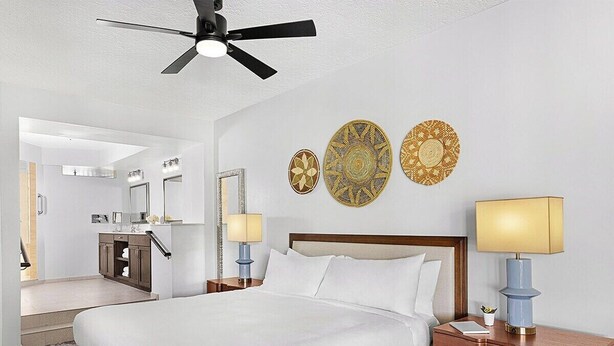 Ein Hotelzimmer mit Bett, Nachttischen, Deckenventilator und dekorativen Wandbildern.