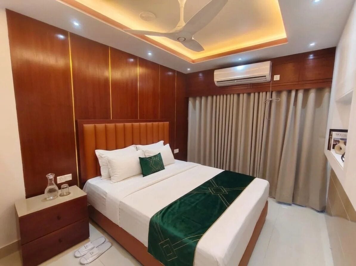 A hotel room with a bed, nightstand, and an air conditioning unit.