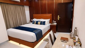 Quarto de hotel com cama, mesa de cabeceira e escrivaninha com cadeira.