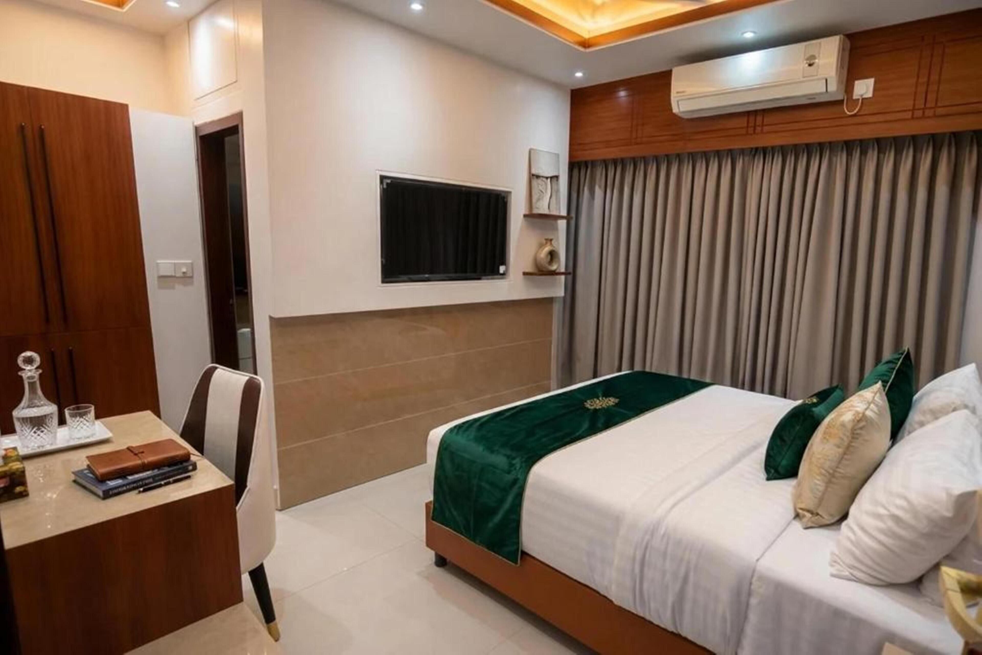 Une chambre d’hôtel comprenant un lit, un bureau, une chaise, un téléviseur fixé au mur et une fenêtre avec des rideaux.