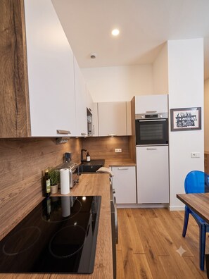 A modern kitchen with wooden cabinetry, a built-in oven, a sink, and a dining area with a blue chair. - Townhouses for 8 people in the Foch neighborhood, 16th arrondissement (Paris)