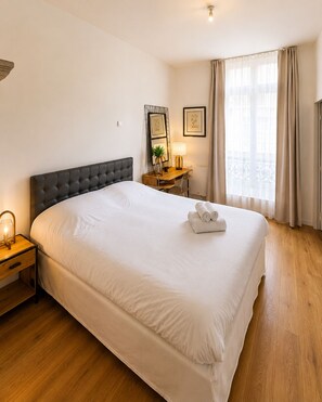 A hotel room with a large bed, a bedside table with a lamp, a desk with a chair, and a window with curtains. - Townhouses for 8 people in the Foch neighborhood, 16th arrondissement (Paris)