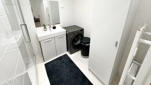 Ein kleines Badezimmer mit einem weißen Waschbecken, einem Spiegel und einer schwarzen Waschmaschine.