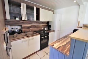 A modern kitchen with white cabinets, a wooden countertop, a built-in oven, and a dishwasher. - Modernly Furnished Double Bungalow With Terrace in the Mirow Holiday Park (Mirow)