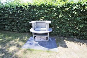 Ein steinernes Outdoor-Barbecue mit flacher Grillfläche und einem Unterschrank für Brennmaterial.
