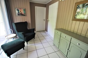 Ein Zimmer mit einem grünen Sessel, einem kleinen runden Tisch, einer grünen Kommode und einer weißen Tür.