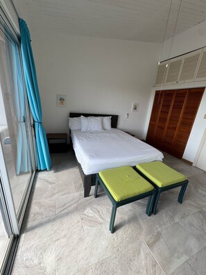 Un dormitorio con cama, banca, armario y ventana con cortinas.