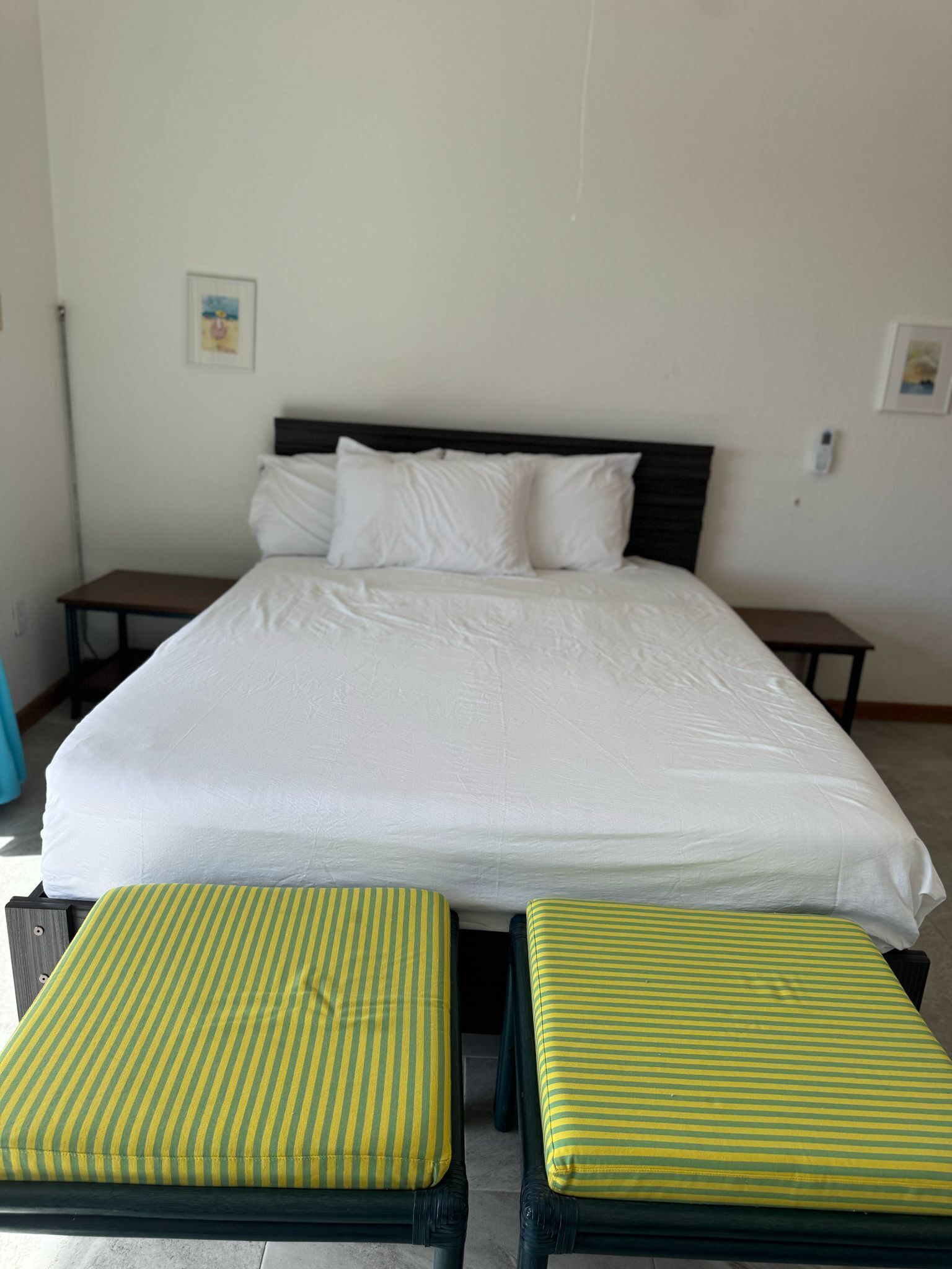 A bed with white bedding, two striped cushions, and a wooden headboard.