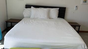 A bed with white bedding, two striped cushions, and a wooden headboard.