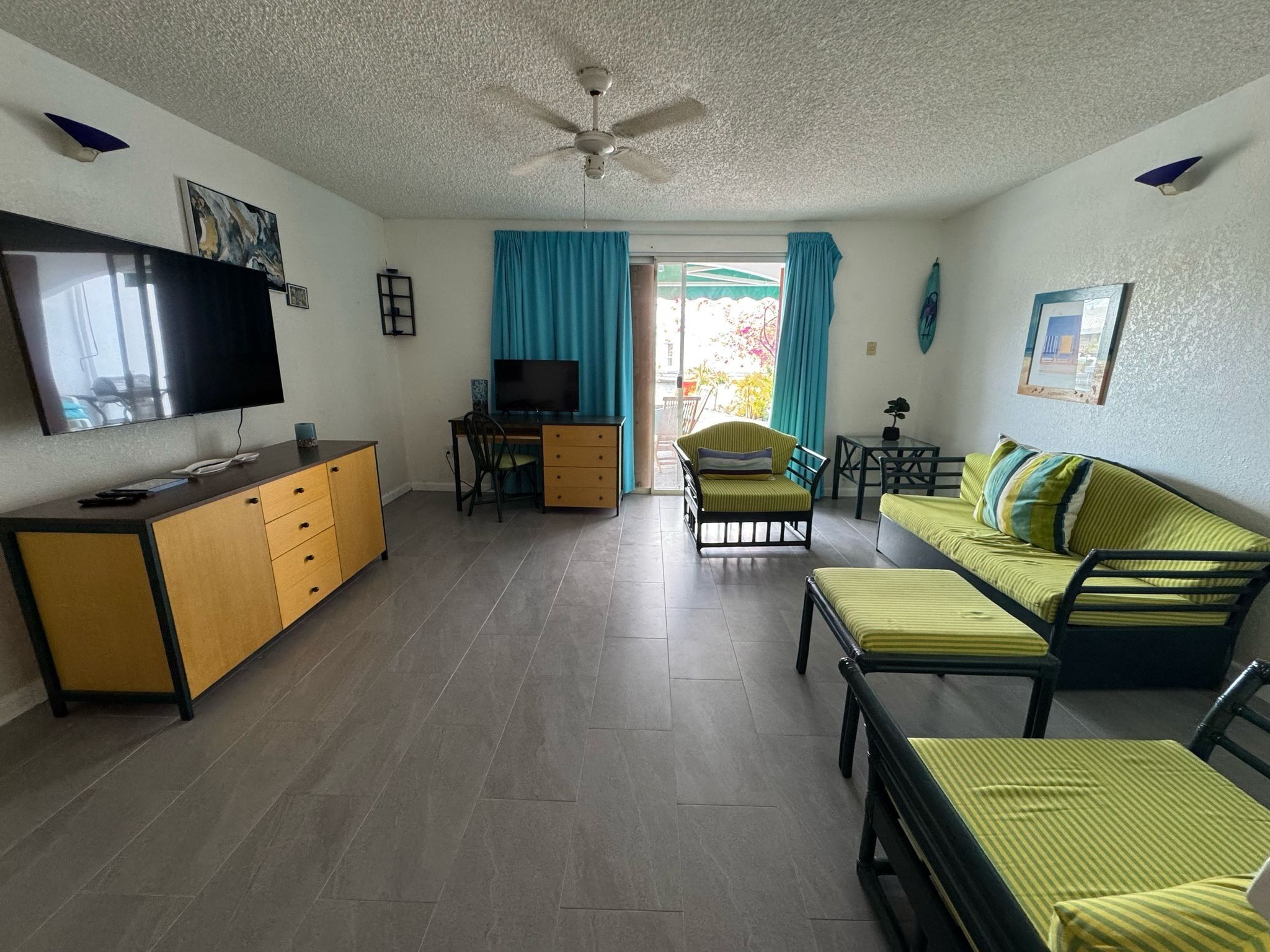 A living room with a television, a desk, a sofa, and a ceiling fan.