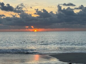 A beach with a sunset, calm sea, and clouds. - Cozy 2-bedroom house in amazing Jolly Harbour with AC (Jolly Harbour)