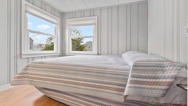 Ein Schlafzimmer mit einem Bett, zwei Fenstern und Blick auf Häuser.