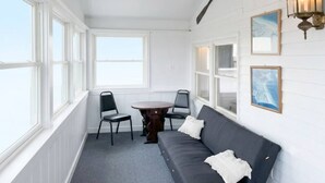 A room with a dark gray sofa, a round table, two chairs, a ceiling fan, and wall-mounted lights.