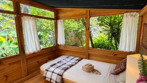 Una habitación de madera con una cama, un tapete blanco y mullido, y una ventana con vistas a la vegetación.
