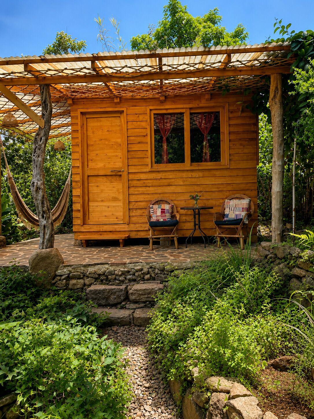 Una cabaña de madera con un porche cubierto, escalones de piedra y dos sillones de mimbre.