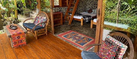 Una terraza de madera con muebles de mimbre, una pared de piedra y un techo de paja.