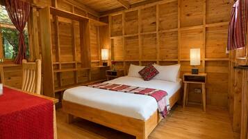 A wooden cabin-style bedroom with a large bed, two bedside tables, a chair, and a hanging light fixture.