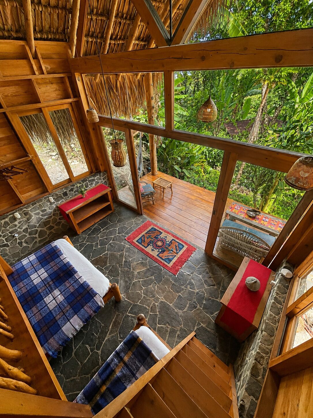 A room with a stone floor, wooden furniture, and a view of lush greenery outside.