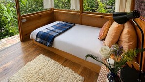 Una habitación con cama, ventana, lámpara y un florero con flores.