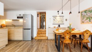 Una cucina moderna con pavimento in legno, forno integrato e frigorifero. C'è un'area pranzo con tavolo e sedie in legno.