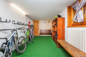 Ein Raum mit grünem Kunstrasenteppich, Holzbanken, einer Holzbank mit Handtuch und einem am Wand montierten Fahrradständer mit Fahrrädern.