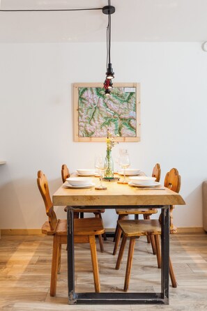 A dining area with a wooden table set for four, surrounded by wooden chairs. A framed map hangs on the wall above the table. - Spacious apartment with 2 bathrooms and a view of the mountains. Large lawn on the property (Teola)
