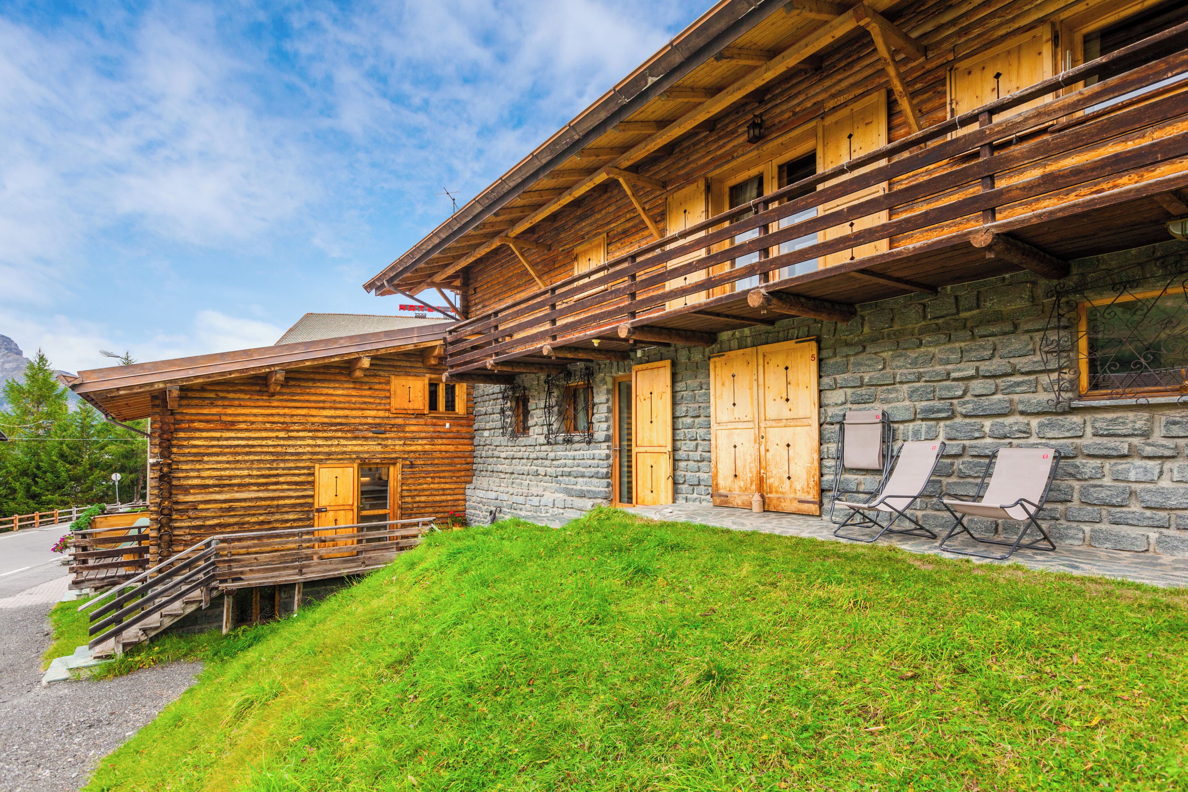 Une cabane en bois avec une façade en pierre, des balcons en bois et un espace salon extérieur.
