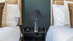 Ein Hotelzimmer mit zwei Betten, einem Nachttisch mit Lampe und einer Schublade.