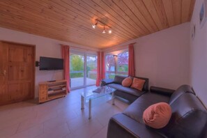 Ein Wohnzimmer mit Holzboden, einer Couch, einem Glastisch und einem Fernseher an der Wand.
