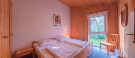 A wooden-framed bed in a room with a white brick wall, a small table, and a chair.