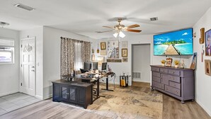 A room with a ceiling fan, a TV on the wall, a desk with a computer, a dresser, and various framed pictures. - Jax and Relax: 3-bedroom house in Jacksonville (Jacksonville)