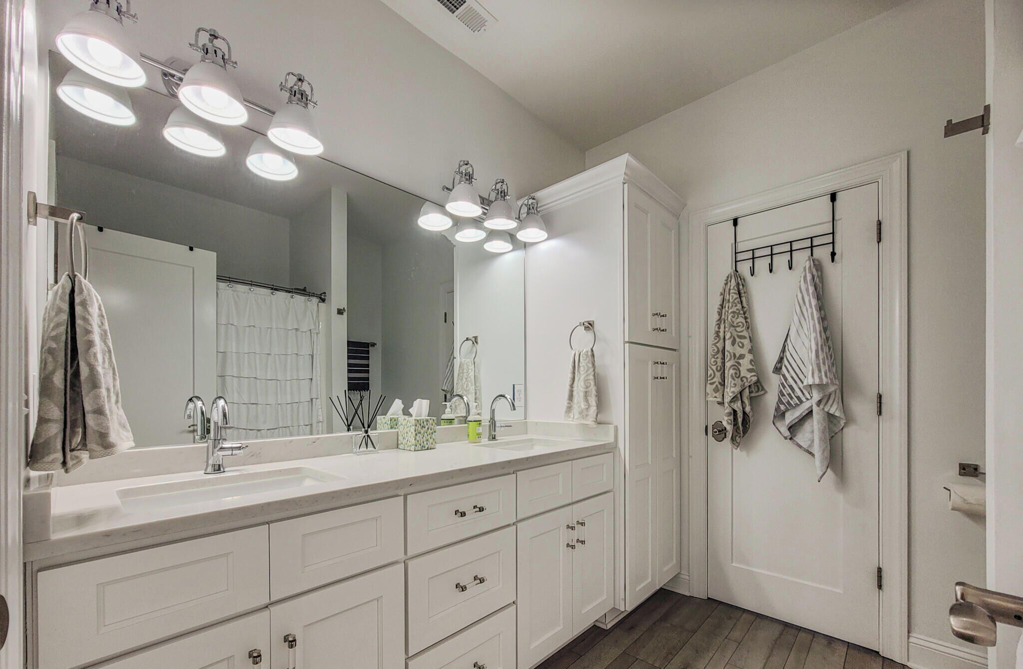 A bathroom with a large mirror, white cabinets, a sink, and a towel rack.
