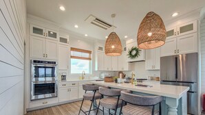 A modern kitchen with white cabinetry, stainless steel appliances, and a central island with bar stools. - La Vie En Bleu - Oceanview Luxury Escape (Surf City)