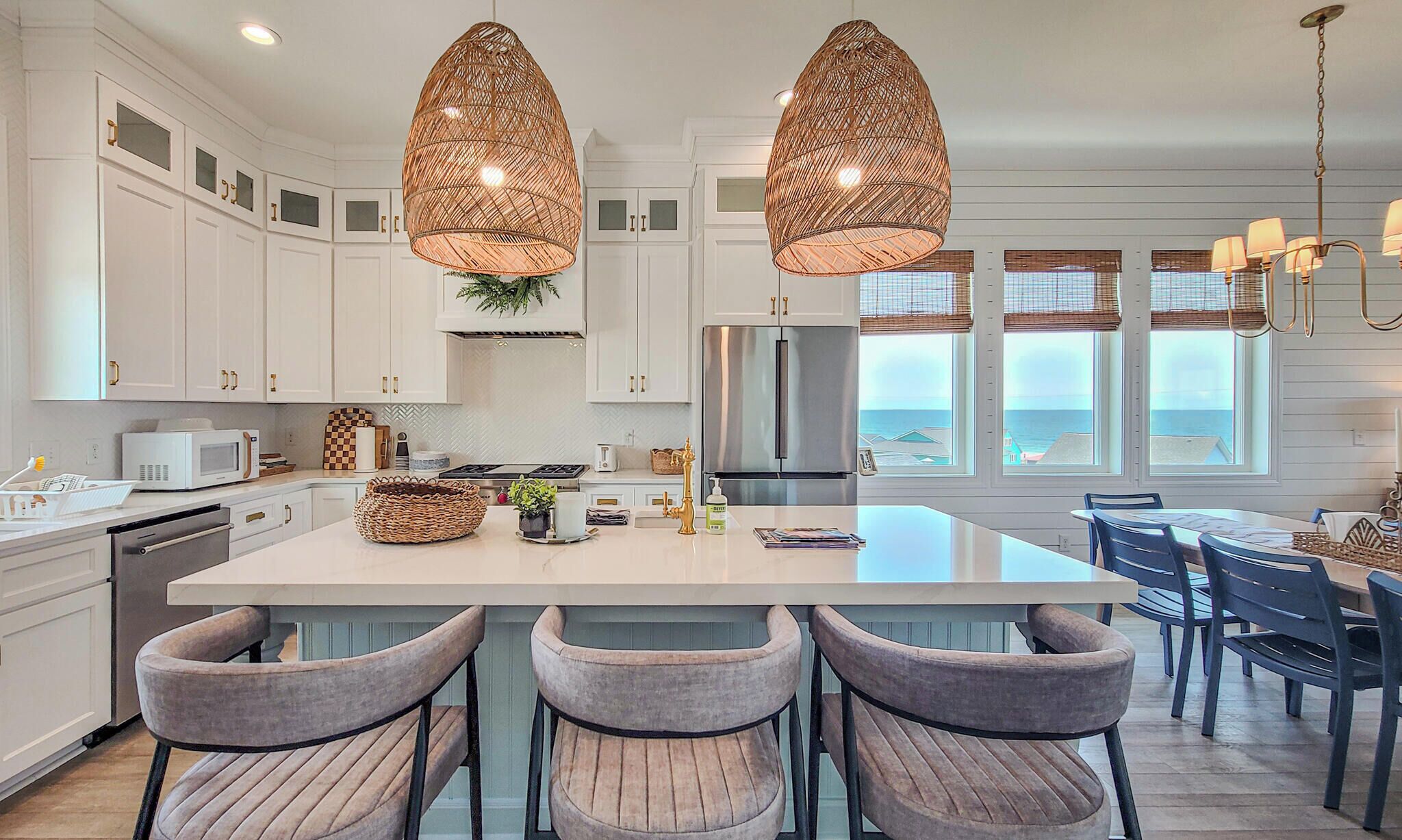 A modern kitchen with white cabinetry, a central island with bar stools, and large windows overlooking the ocean.