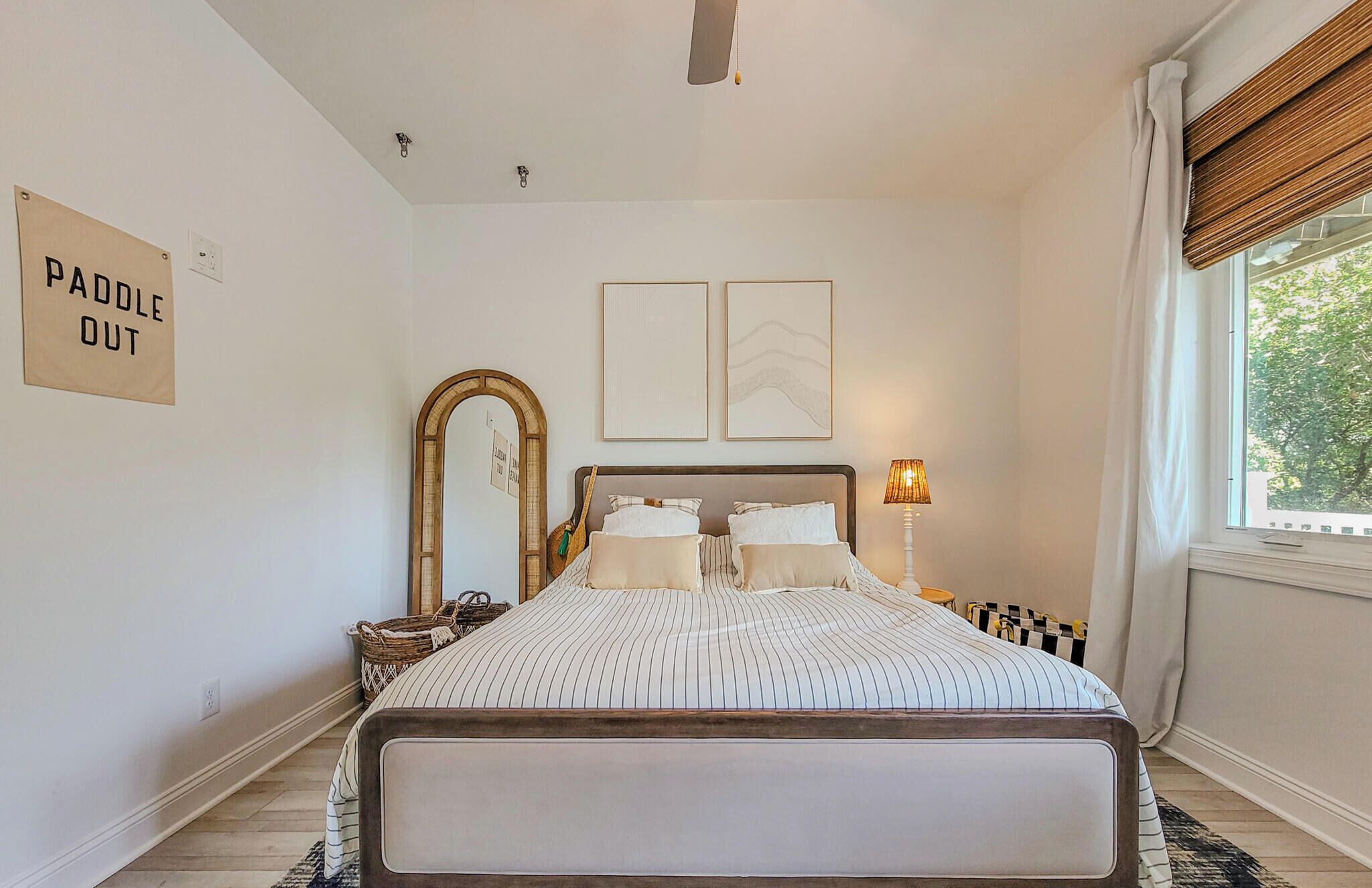 A bedroom with a bed, a mirror, a lamp, and a window with curtains.