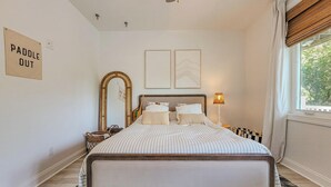 A bedroom with a bed, a mirror, a lamp, and a window with curtains. - La Vie En Bleu - Oceanview Luxury Escape (Surf City)