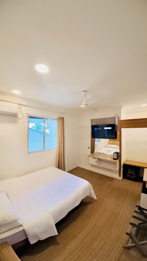 Quarto de hotel com cama, televisão, janela e ventoinha no teto.