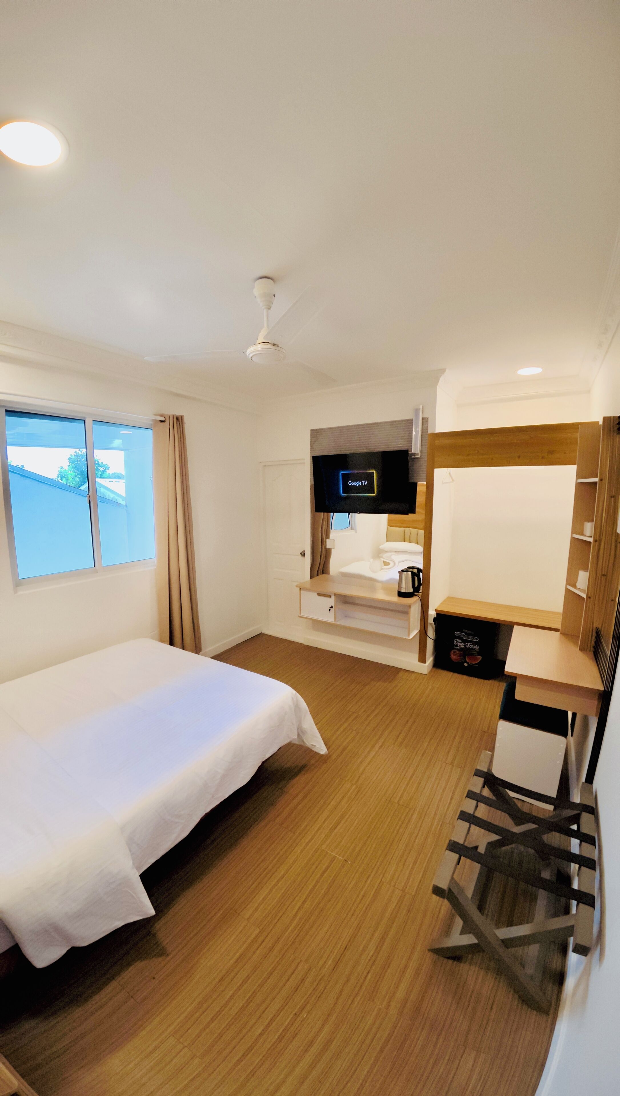 Habitación de hotel con cama, escritorio y silla, televisor y ventana con cortinas.