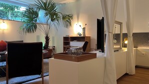 A modern living room with a large window, a potted palm tree, a wooden coffee table, and a white sofa.