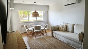 Een moderne woonkamer met een eettafel met glazen blad, witte banken en een groot raam met uitzicht.