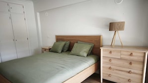 Een slaapkamer met een bed, nachtkastje, dressoir en lamp.