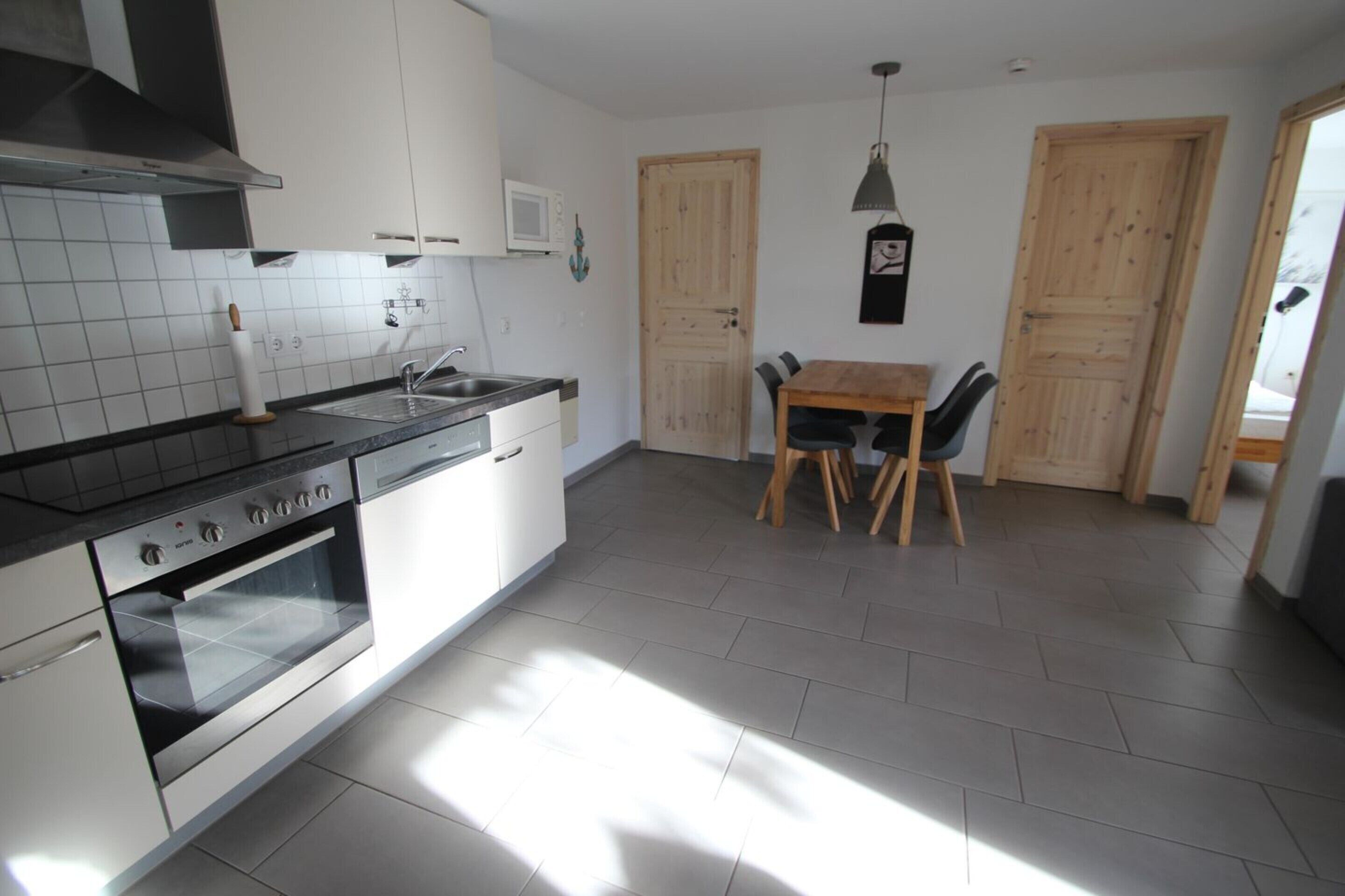 Een moderne keuken met een inbouwoven, een spoelbak en een eethoek met een houten tafel en stoelen.