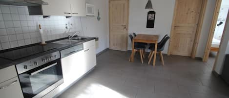 Una cocina moderna con horno empotrado, un lavamanos y una zona de comedor con mesa y sillas de madera.