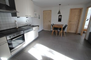 A modern kitchen with a built-in oven, a sink, and a dining area with a wooden table and chairs. - Moderner Bungalow mit Terrasse im Ferienpark Mirow (Mirow)