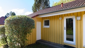 Um edifício amarelo com telhado de telhas vermelhas, uma pequena janela e uma porta.