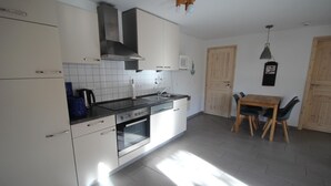 Uma cozinha moderna com armários brancos, forno embutido, micro-ondas e um espaço de refeições com mesa e cadeiras de madeira.