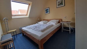 Un dormitorio con una cama individual, un escritorio, una silla, una mesita de noche con una lámpara, una ventana y dos cuadros en la pared.