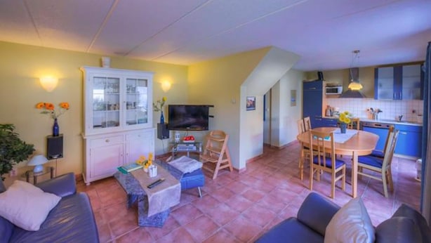 Un espacio habitable compacto con sofá, mesa de comedor, televisor y zona de cocina.
