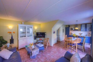 A compact living space with a sofa, a dining table, a TV, and a kitchen area. - Gemutliches Ferienhaus mit Garten im Hafendorf Muritz in Rechlin (Rechlin)