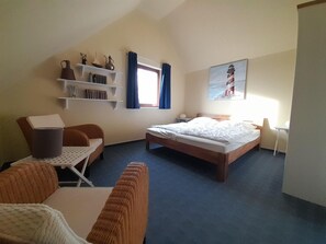 A hotel room with a bed, a chair, a small table, a bookshelf, and a painting on the wall. - Gemutliches Ferienhaus mit Garten im Hafendorf Muritz in Rechlin (Rechlin)